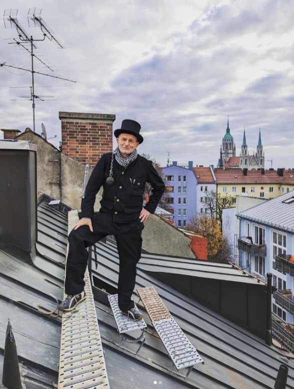 Hans Ritt in Kaminkehrer Arbeitskleidung auf einem Dach - Münchner Frauenkirche im Hintergrund